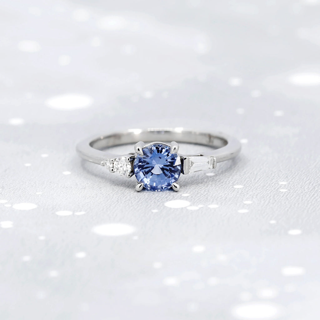 Splendid engagement ring handmade by independent jewelry designer Justine Quintal in Montreal. Made in white gold with a splendid round-shaped light blue sapphire, this ring is composed of baguette diamonds arranged asymmetrically to give an original and elegant style. This alternative bridal jewelry is made in Canada and is available at Ruby Mardi, a jewelry store specialized in creations from Canadian jewelry artisans.