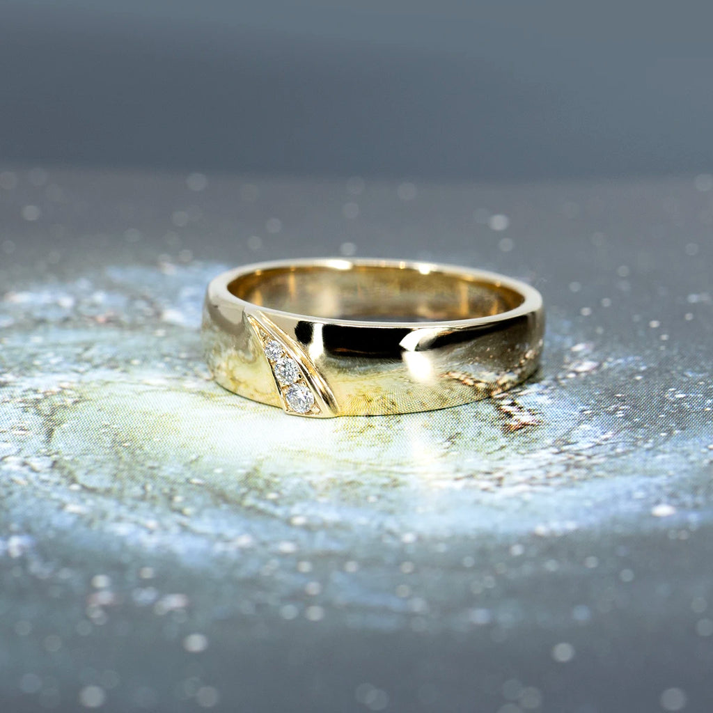 Close-up view of a yellow gold wedding band with three diamonds arranged in the shape of a shooting star, handcrafted by Toronto designer Yuliya Chorna, and available exclusively at Ruby Mardi in Montreal. The gold ring is seen photographed on a picture of the milky night.