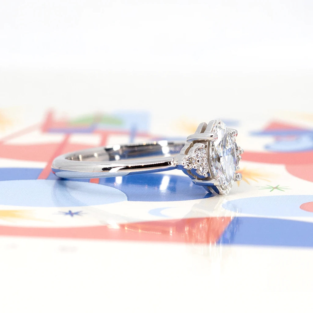 Side view on a colorful background of an icy engagement ring. The jewel is in white gold and presents a central marquise diamond with 3 small round brilliant diamonds on each side.