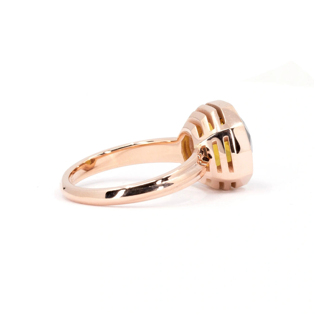 Seen from the side: a funky rose gold ring with geometrical openings in the basket. We can't see a yellowish gemstones trough the openings. It's a bold cocktail ring designed by Canadian brand Bena Jewelry.