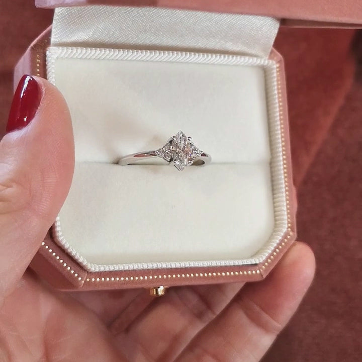 8 seconds video with a funky music presenting an all diamond white gold engagement ring in a pink velvet box that is held by a woman's hand with red fingernails.