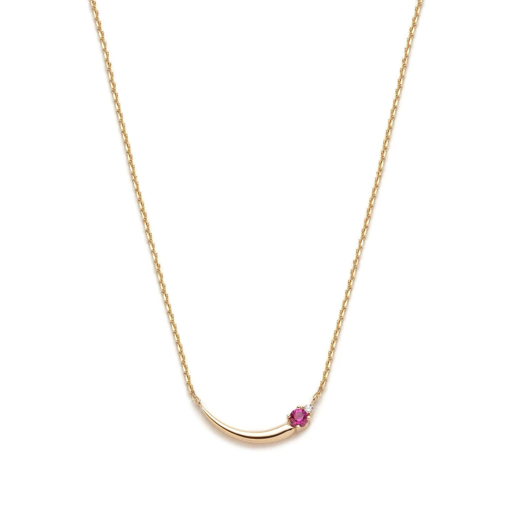 A feminine and asymmetrical gold necklace seen photographed on a white background. The piece of jewelry shows a curved gold detail, a pink tourmaline et a small round brilliant diamond.