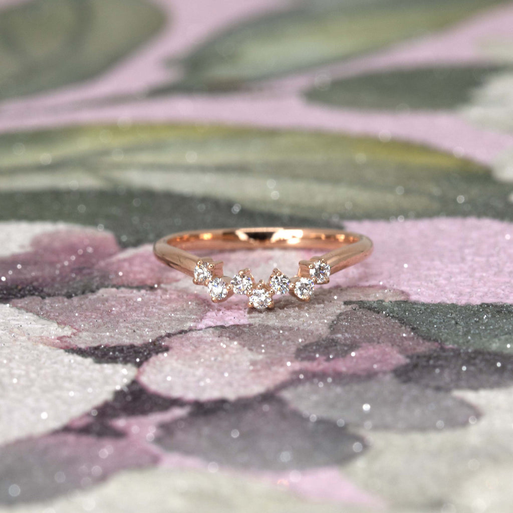 Jonc de mariage en or rose avec sept diamants photographié sur un papier peint fleuri et brillant.