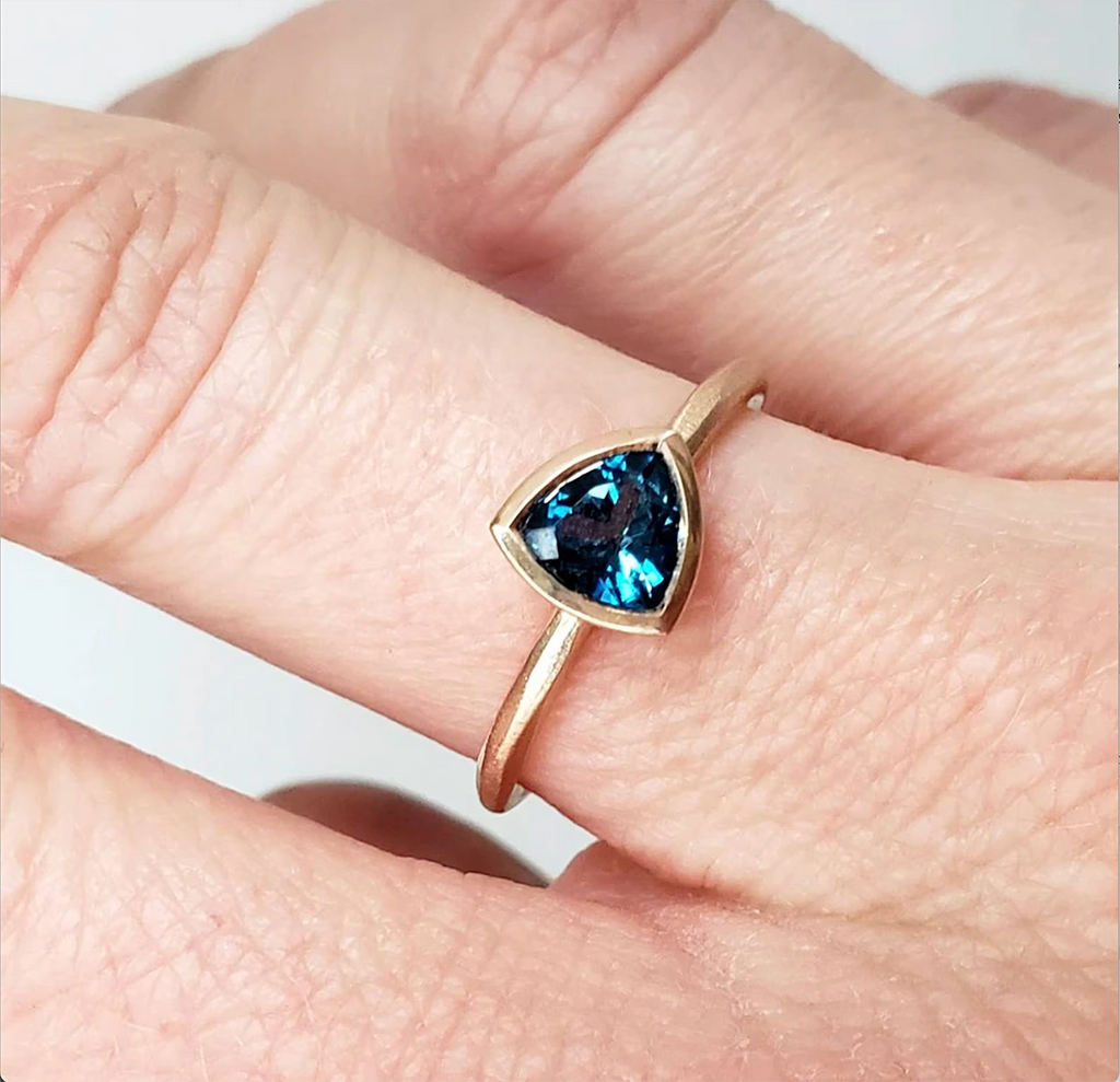 girl wearing trillion shape london blue topaz bezel setting yellow gold bridal ring made in montreal little italy jeweler boutique ruby mardi on a white background