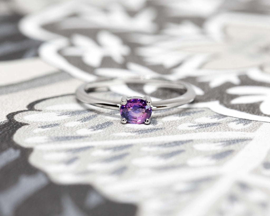 A magical two colours sapphire with pink and purple hues, set in 14k white gold and photographed on a wallpaper. Beautiful, simple and elegant solitaire engagement ring.
