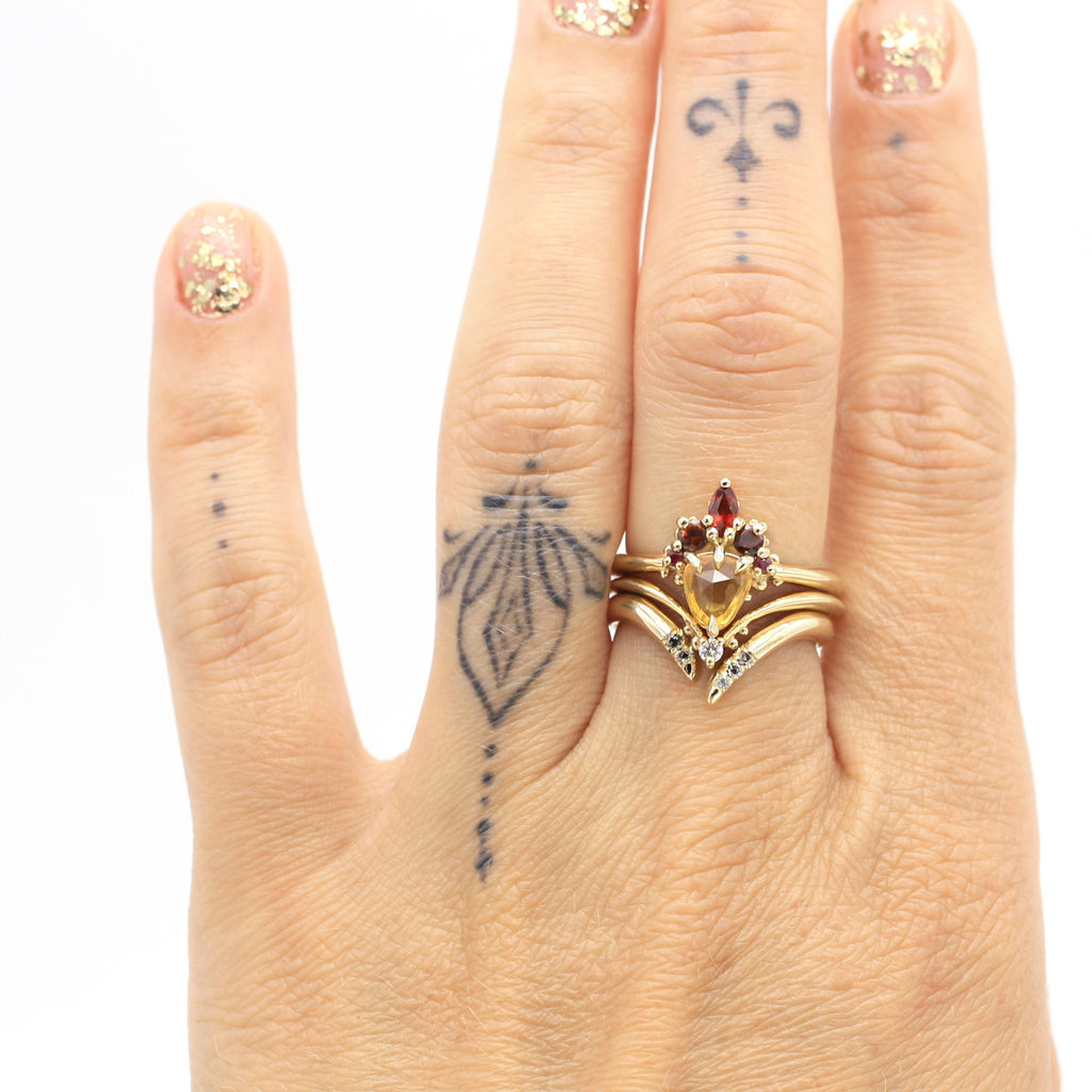 A hand is wearing a stunning and colourful engagement ring and two wedding bands in V shape with diamonds. Find Nadia Werchola’s creation at high end jewelry store Ruby mardi in Montreal’s Little Italy.