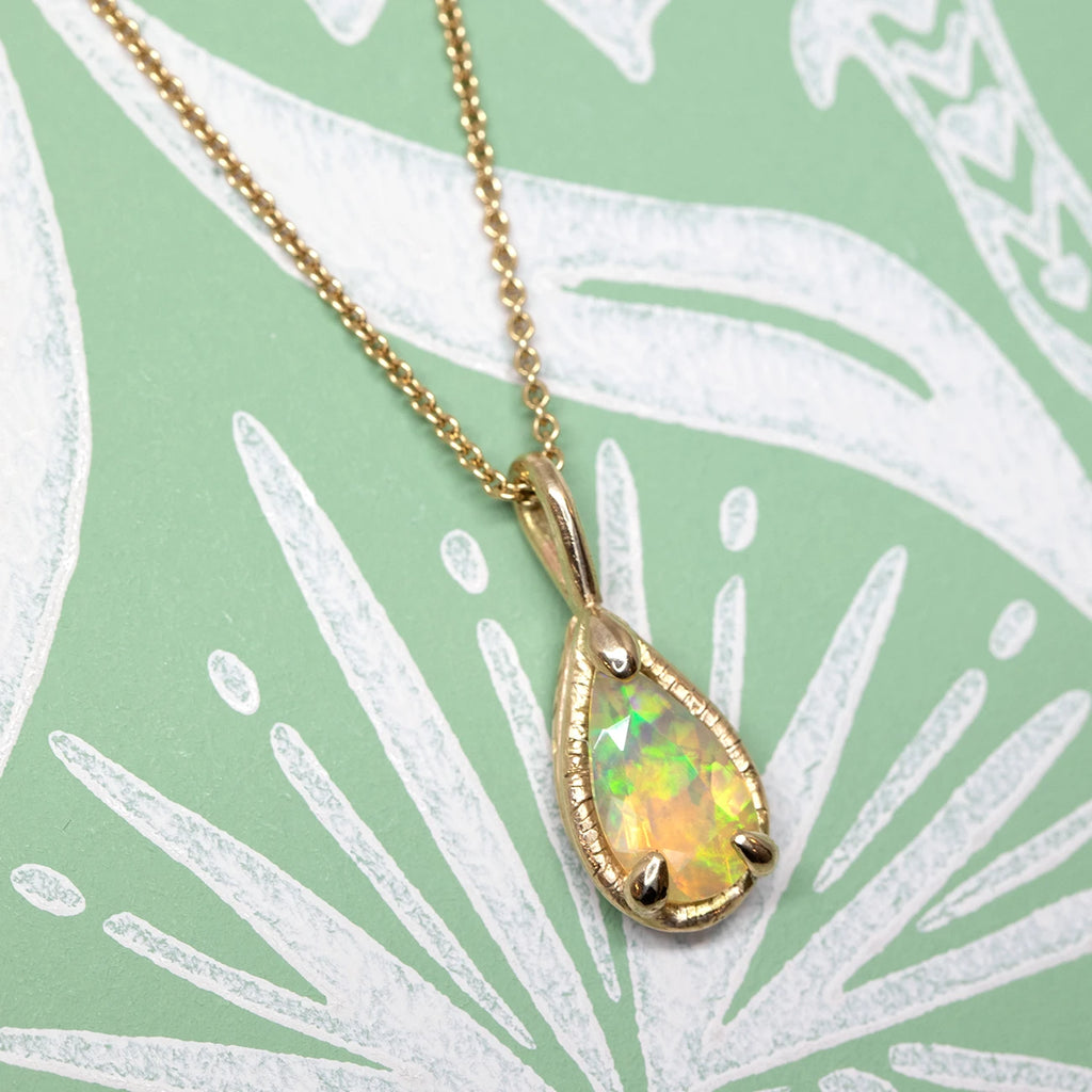 side view of pear shape opal pendant yellow gold custom made jewelry design sheena on a green and white background