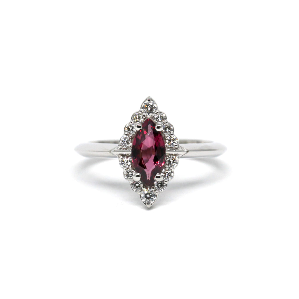 A beautiful engagement ring seen on a white background. This red raspberry garnet is surrounded by a round brilliant diamond halo. This handmade ring has a vintage look with a modern touch. Find it online or at our fine jewelry store in Montreal.