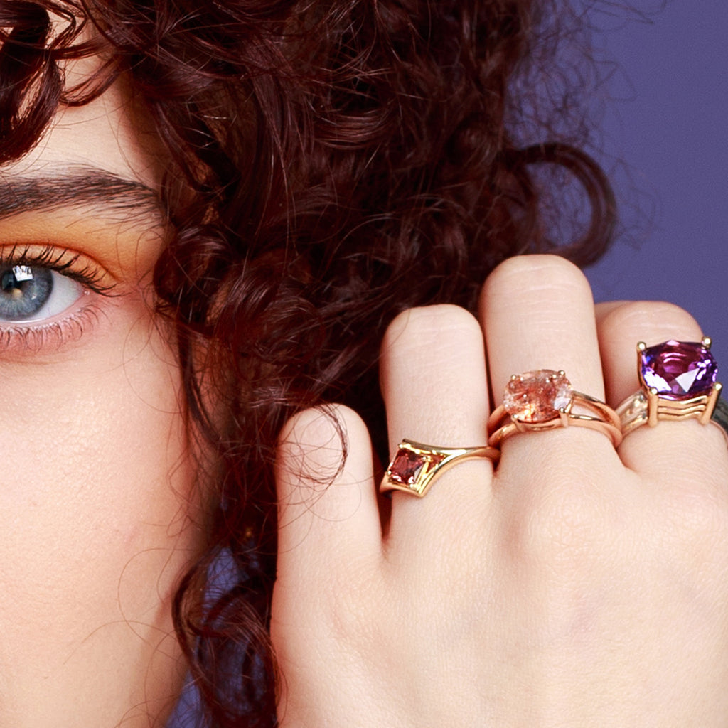 Three stunning statement rings by Canadian jewelry designer BENA JEWELRY, worn by a lady seen in close-up. A huge amethyst ring, a rose gold sunstone ring and a peach zircon yellow gold ring. Find them all at high end jewelry store Ruby Mardi in Montreal.