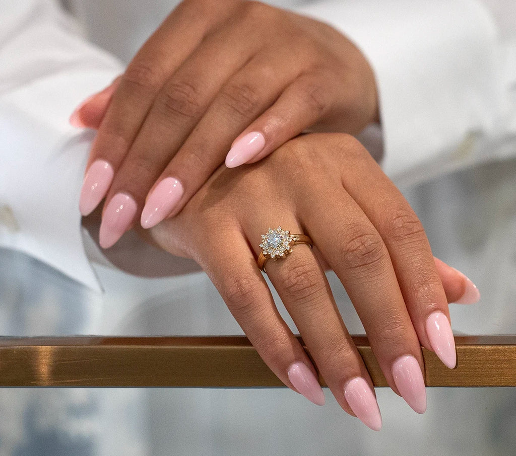 Two elegant lady's hands with long pink nails wear a big lab grow diamond engagement ring in a sun shape.
