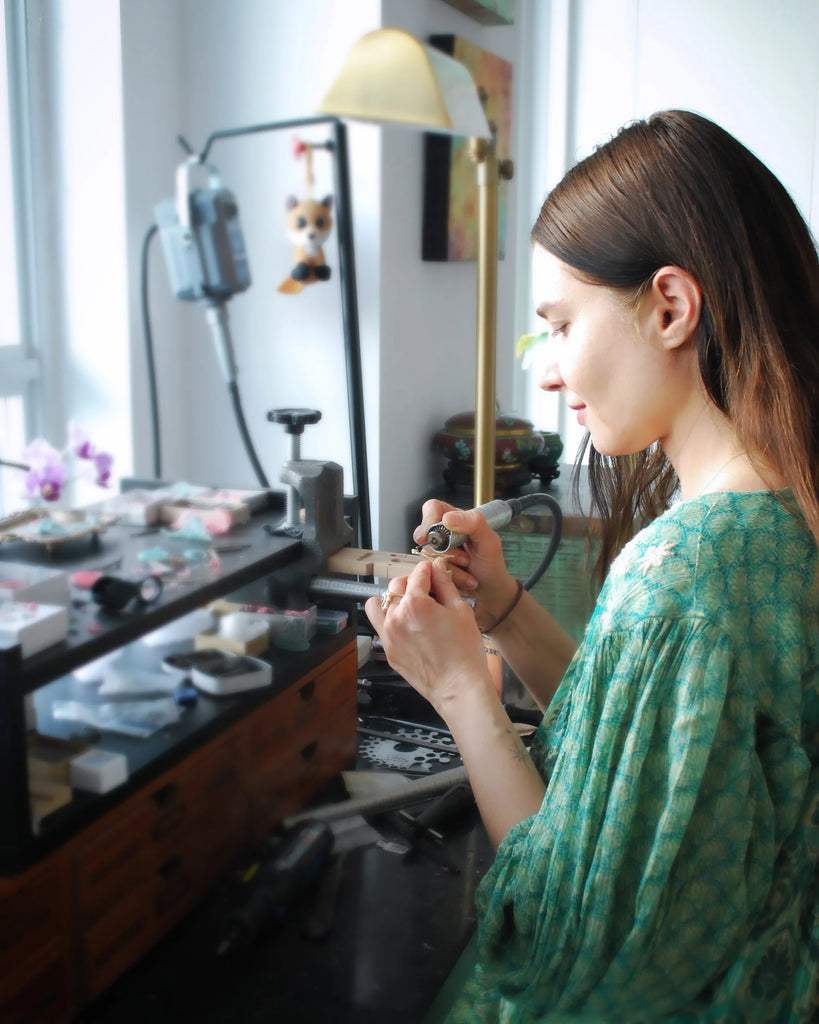 A young Canadian jeweller works at her bench and wears a green dress. Her name is Anat Kaplan.