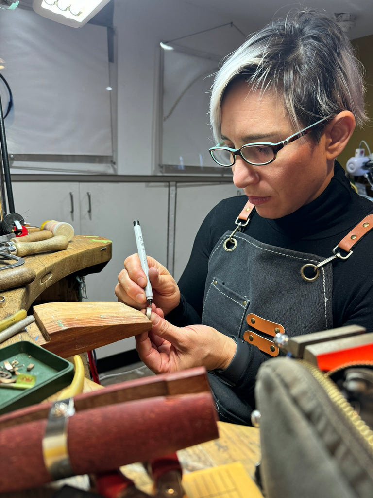 A young lady with short hair and glasses makes a mark on a ring before she will work on it. She is sited at her jewelry bench, she is a Canadian jeweller.