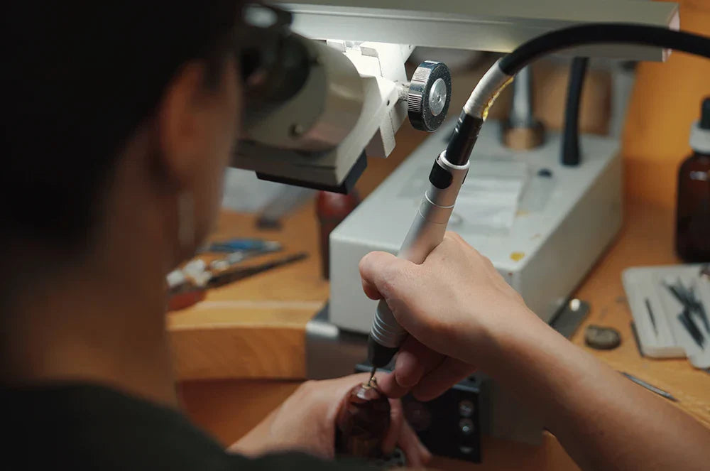 A woman setting a jewel is photographed from behind at her work table.