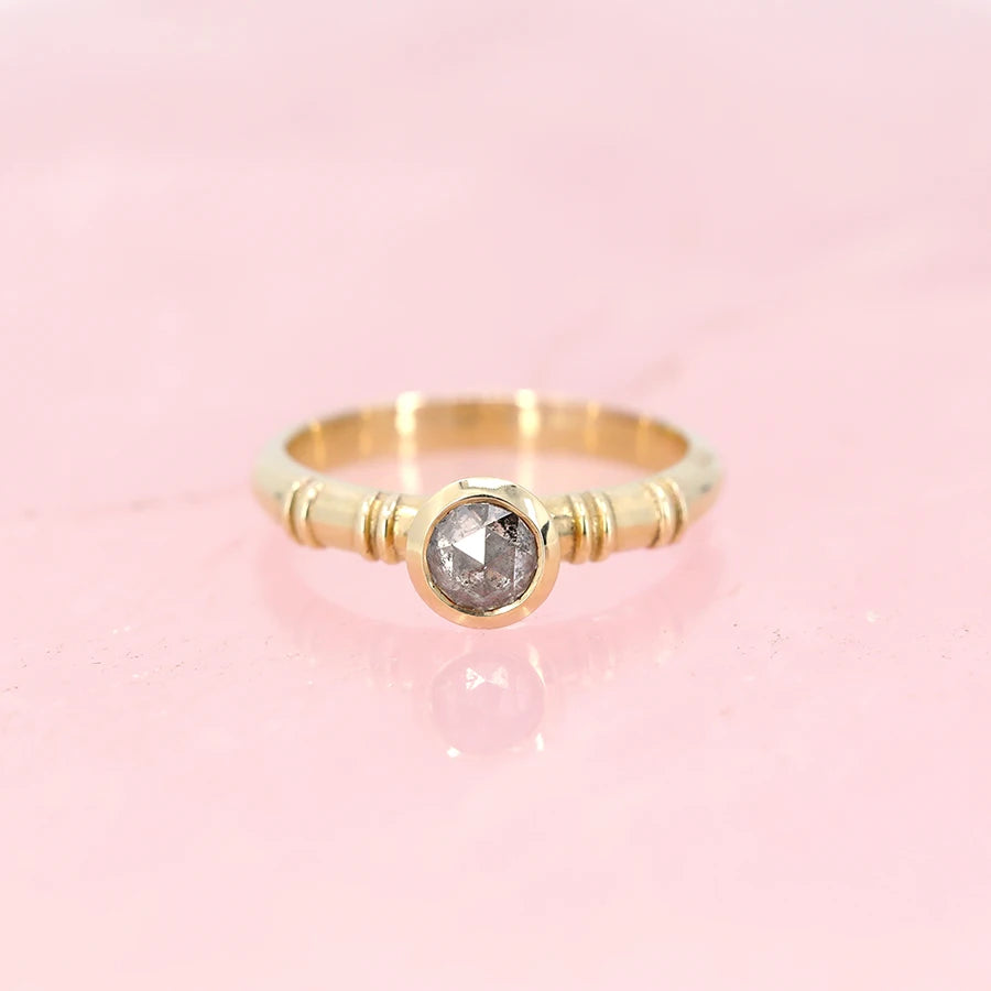 One-of-a-kind yellow gold ring with an ancient vibe featuring a round rose cut salt and pepper diamond photographed on a rose quartz background. An alternative engagement ring available at Ruby Mardi. 