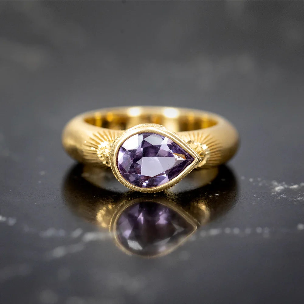 Gold ring by K and Co Bespoke featuring a pear-shaped lavender sapphire set in a bold sculptural band with engraved radiating details. Handcrafted in Toronto and photographed at Ruby Mardi.