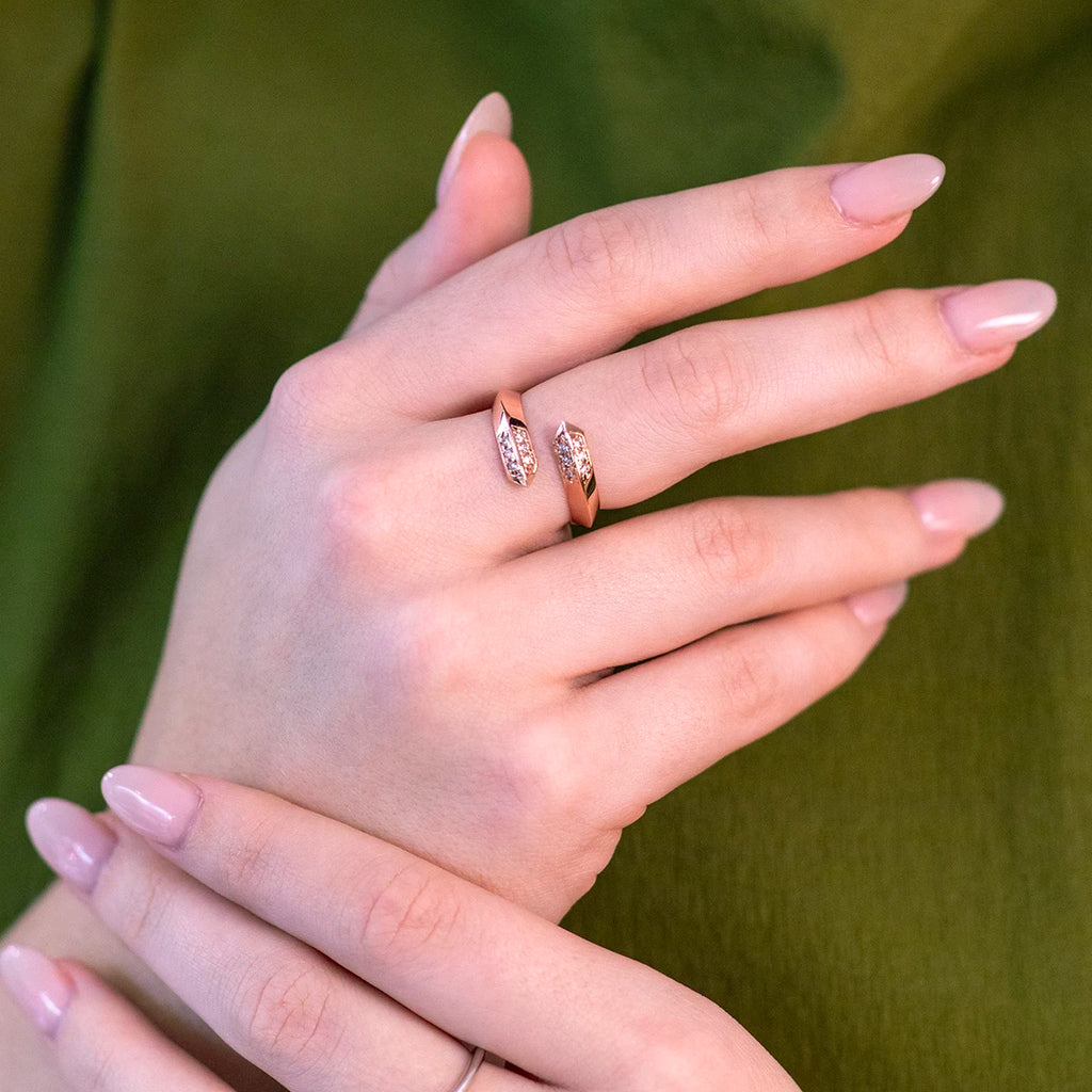 14kt rose gold wrap ring worn on a hand with light pink nails, complemented by a dark green dress. The lab-grown diamonds at each end of the ring add a touch of elegance and sparkle.