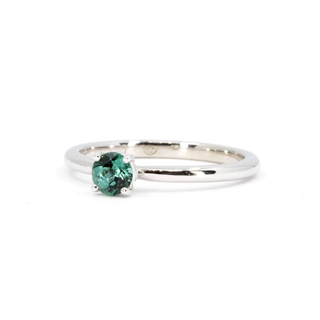 Side view of a 18k white gold ring featuring a dainty natural round  green tourmaline. This classic solitaire engagement ring with a green gemstone is available at Montreal jewelry store Ruby Mardi, and was handmade by indie brand Atelier Emigé.