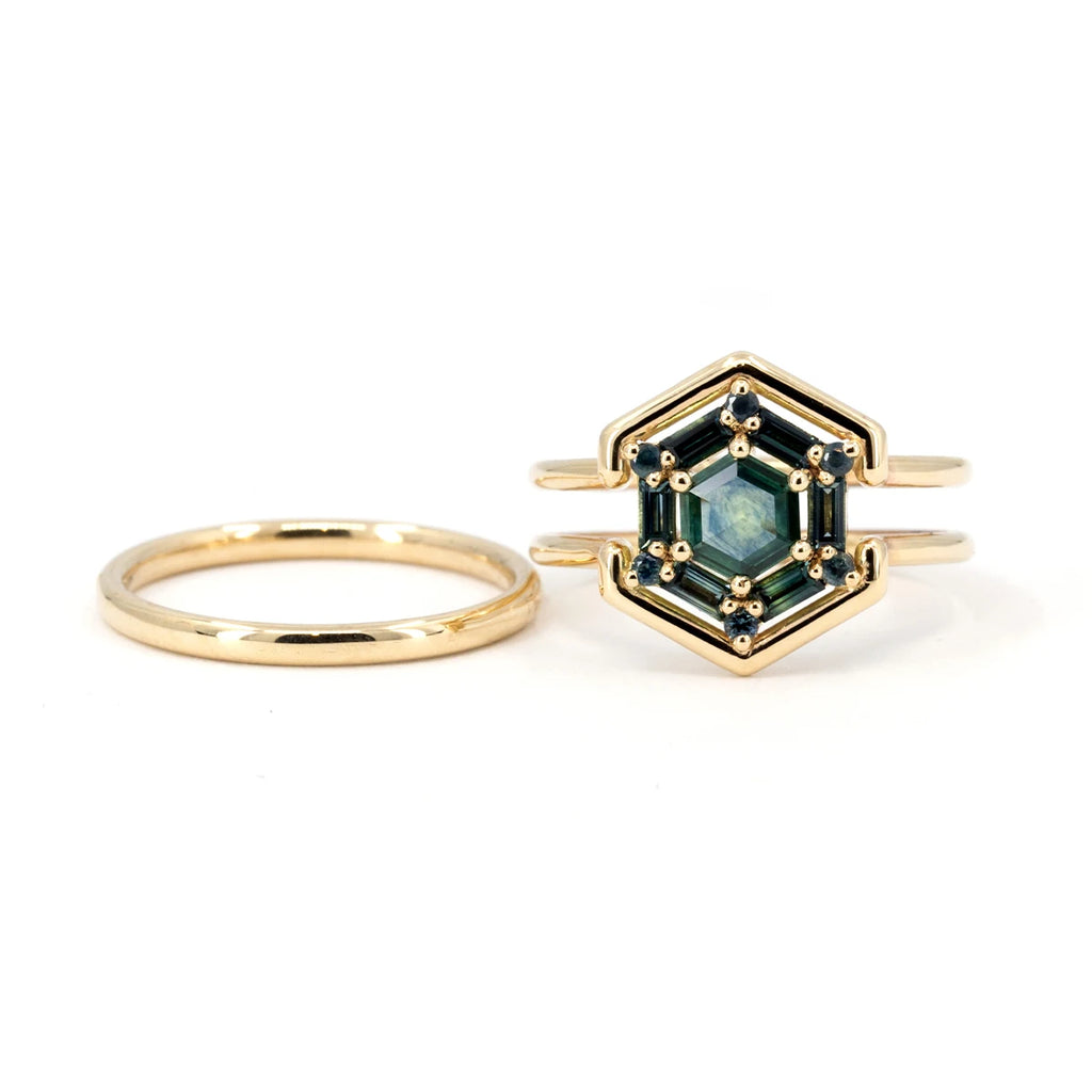 A ring with a unique design is photographed against a white background, from the front: the ring is made of yellow gold and offers a 2-in-1 design: a wedding band fits inside the main gauge, which can double as an engagement ring. Here we see the ring removed from the main band. It features 13 natural sapphires in shades of blue and green (teal), the whole forming a hexagonal shape. Created by Vancouver-based Erica Leal. This fine jewel is available at Canadian fine jewelry store Ruby Mardi.