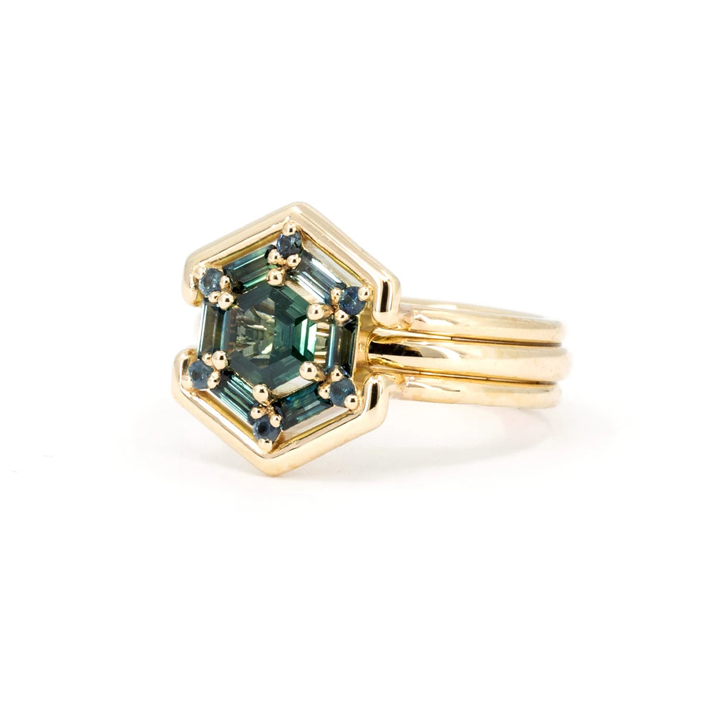 Side view of a large, funky and stylish yellow gold ring photographed against a white background.  It features 13 natural sapphires in shades of blue and green (teal), the whole forming a hexagonal shape. Created by Vancouver-based Erica Leal. This fine jewel is available at Canadian fine jewelry store Ruby Mardi.