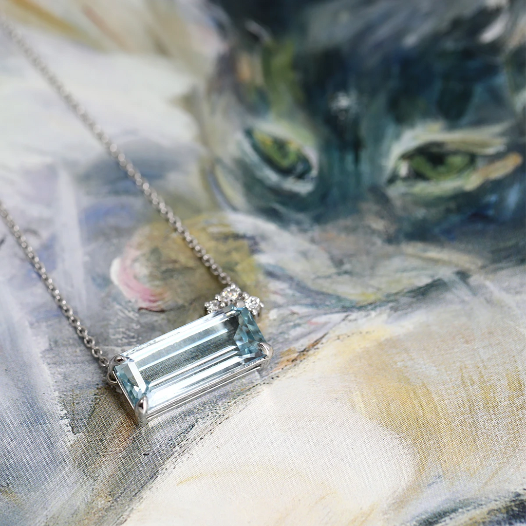 Close-up of a handmade 14k white gold necklace by designer Justine Quintal, featuring a 4-carat emerald-cut aquamarine accented with delicate diamonds, resting on an artful background. Available exclusively at Ruby Mardi, Montreal’s coolest jewelry store.