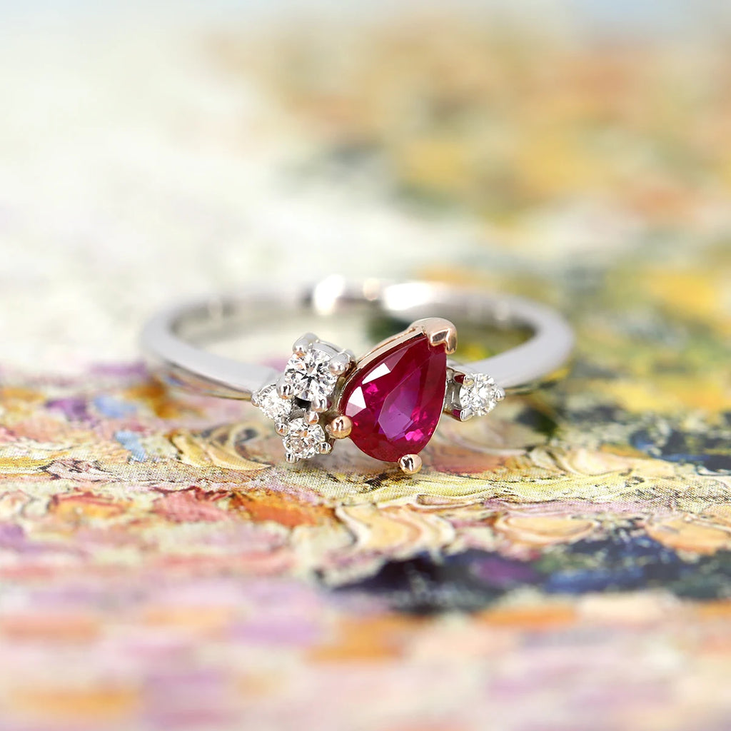 A bridal jewel photographed on a colorful background. The alternative engagement ring is set in white gold and rose gold and features a natural pear shape ruby with natural diamond accents. This wedding ring was handcrafted by Justine Quinal and is available only at Ruby Mardi, the best jewelry store in Montreal.