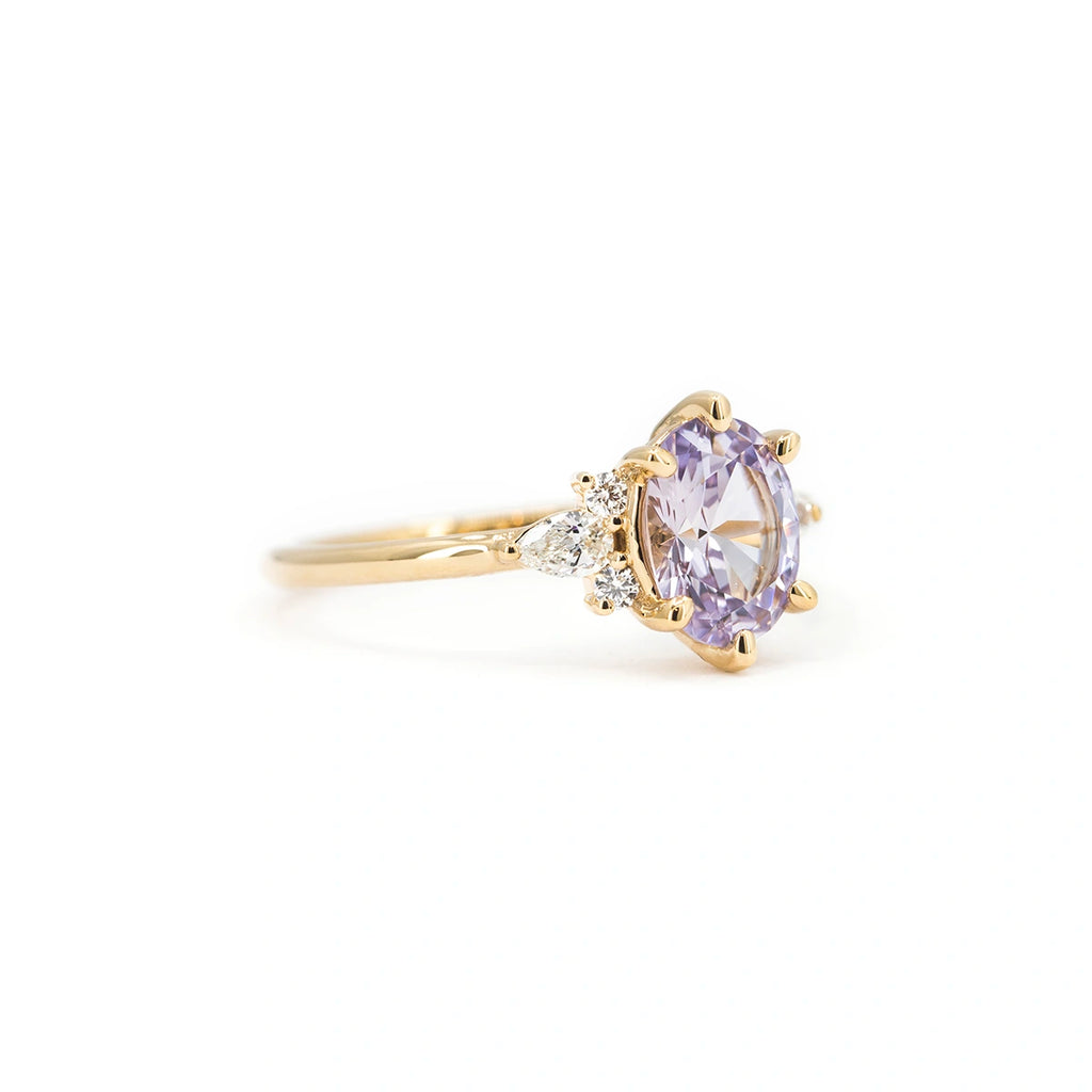 Side view of lilac sapphire engagement ring with pear and round diamond accents in 14k yellow gold. Handmade in Montreal by Maksym Jewelry for Ruby Mardi.