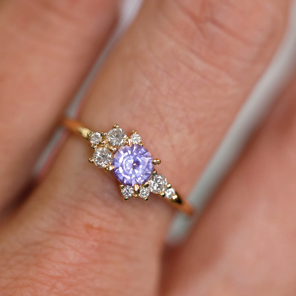 Light purple unconventional engagement ring with an asymmetrical cluster of natural diamonds, handcrafted in Montreal by Justine Quintal, seen worn on a hand in close up.