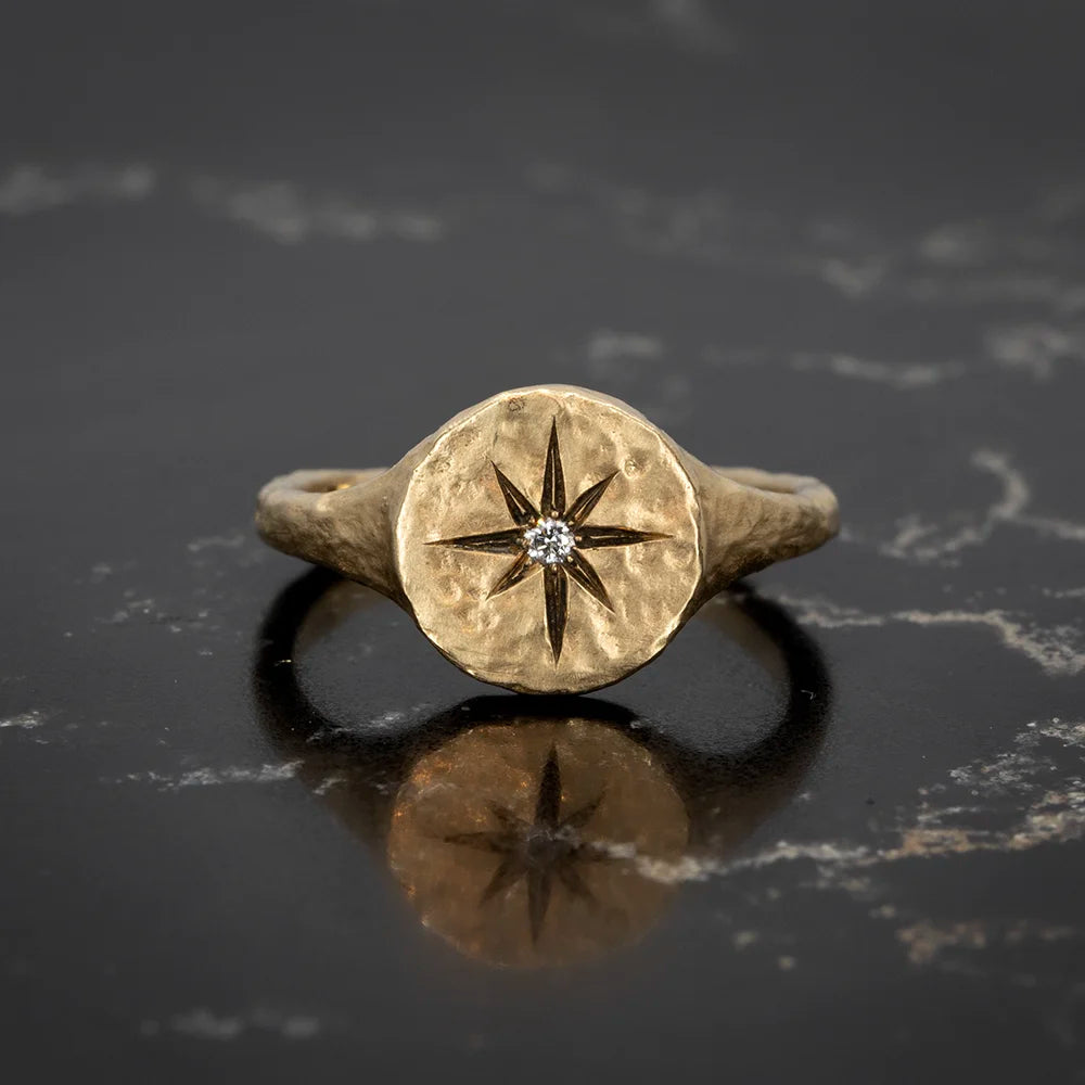 A handcrafted gold ring by Anouk Jewelry, featuring a textured round face engraved with a radiant star design and a central diamond accent. Available at Ruby Mardi in Montreal.