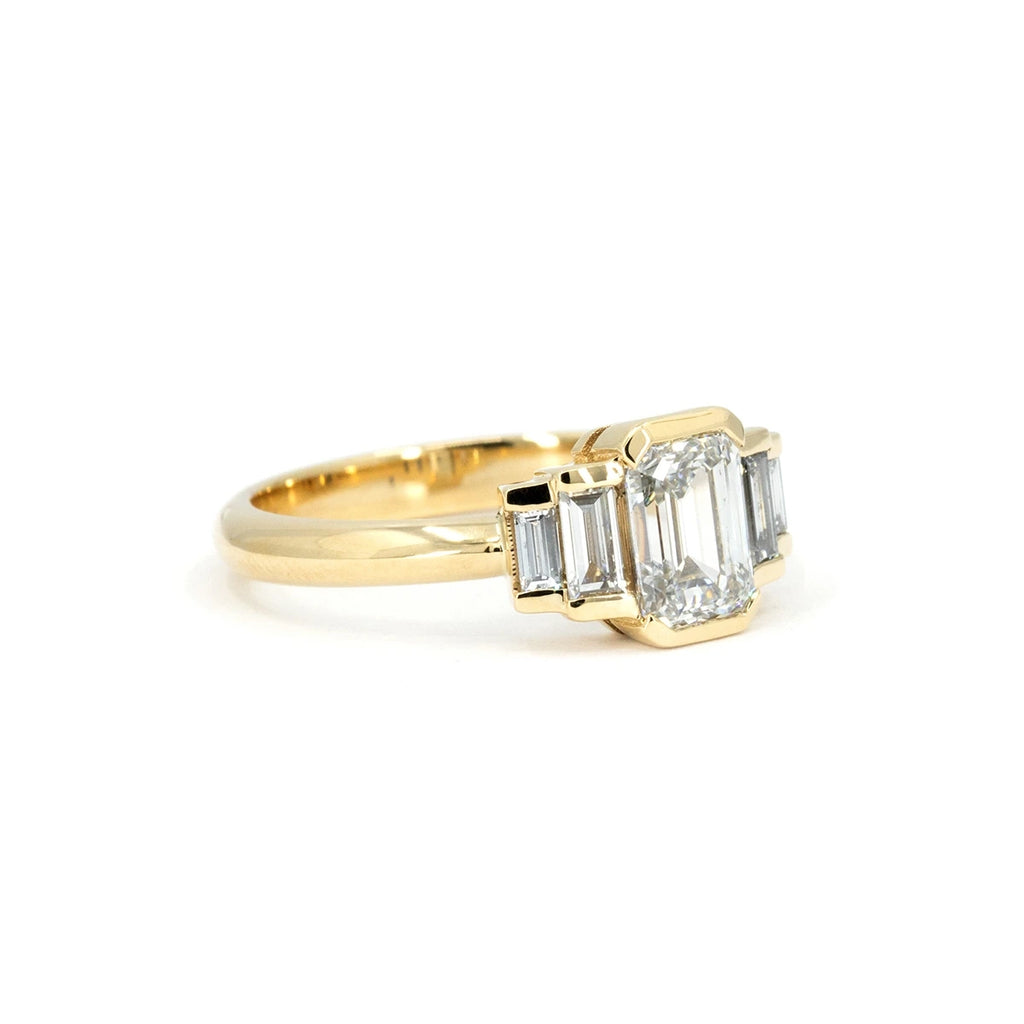 Emerald-cut diamond ring in yellow gold with Art Deco styling. The central emerald-cut diamond is flanked by tapered baguette diamonds on each side. Clean lines and geometric symmetry define this bold engagement ring handcrafted in Montreal by Ruby Mardi.