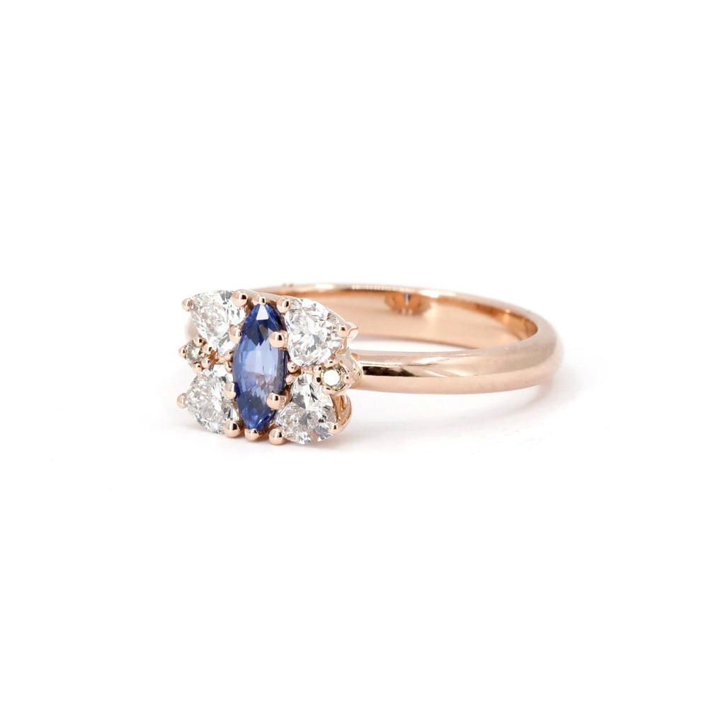 Angled view of the Aurorina sapphire and diamond cluster ring in rose gold, with a vivid marquise blue sapphire centerpiece and white diamond accents. Ruby Mardi fine jewelry.