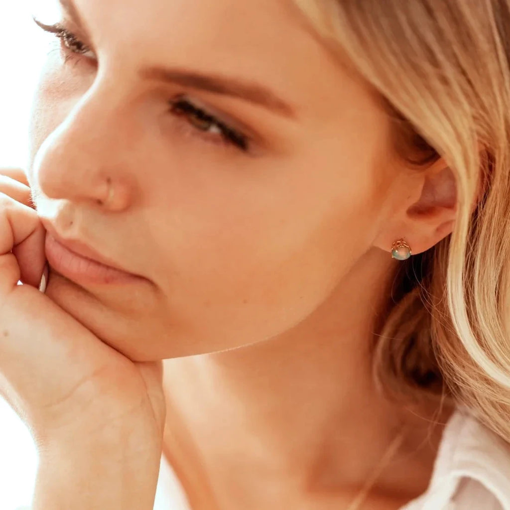Woman wearing oval opal stud earrings in 14k yellow gold with a delicate floral design. Handmade in Canada by Rooz Jewellery for Ruby Mardi, the coolest jewelry store in Montreal.