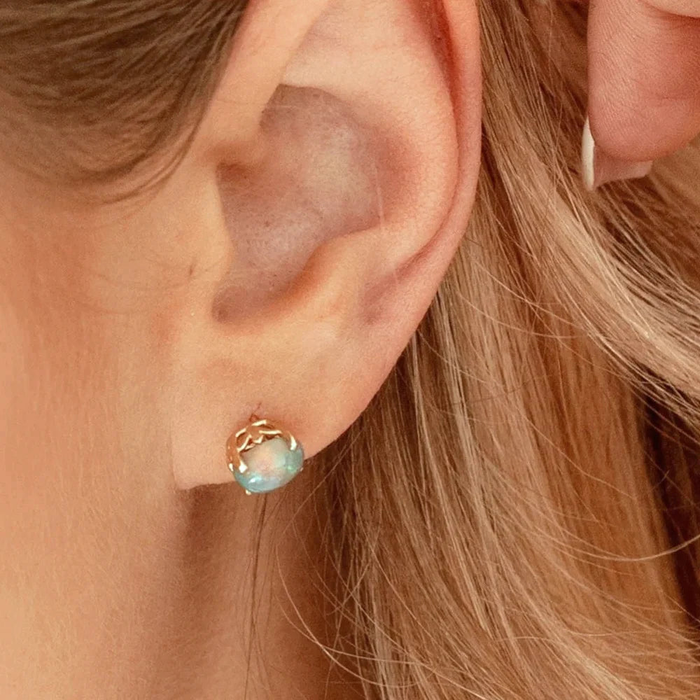 Close-up of an opal stud earring in 14k yellow gold with a floral basket setting, worn on the ear.