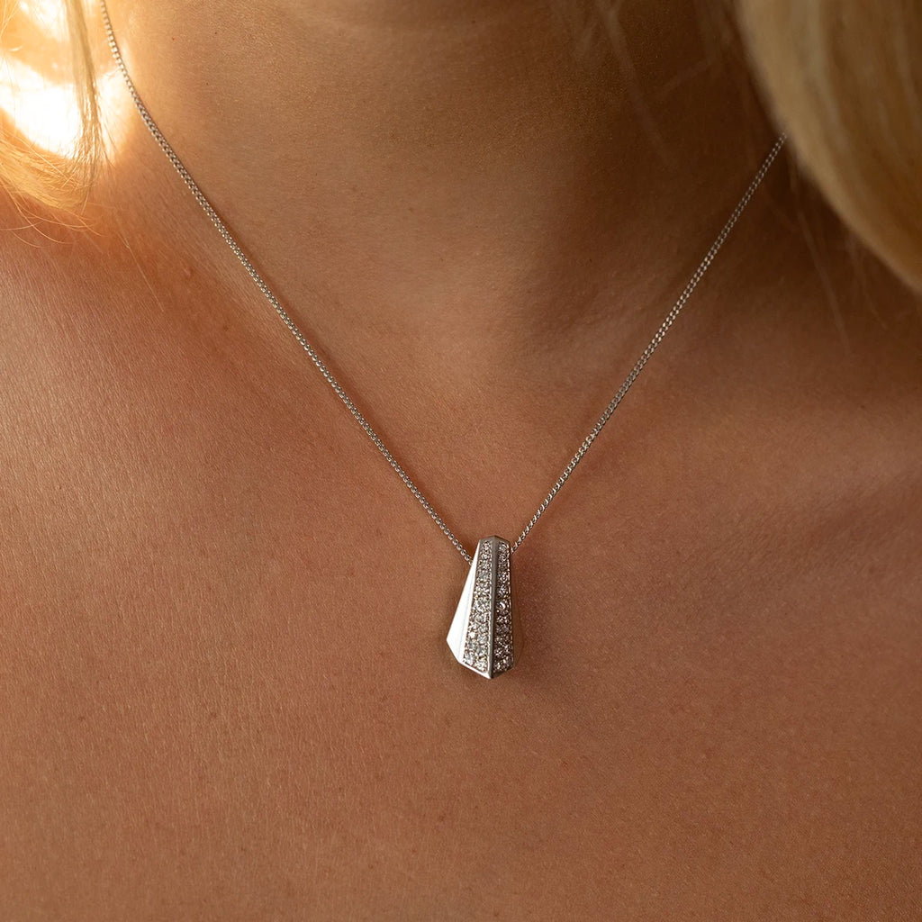 Close-up of a modern 14k white gold pendant with pavé diamonds in an angular, sculptural design. Contemporary fine jewelry piece by Bena Jewelry, available at Ruby Mardi in Montreal.