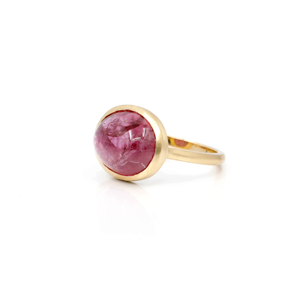 Side view on a white background of a big yellow gold bezel ring. The central stone is a huge natural ruby cabochon showing many interesting inclusions. This designer ring is available in Montreal at Ruby Mardi.