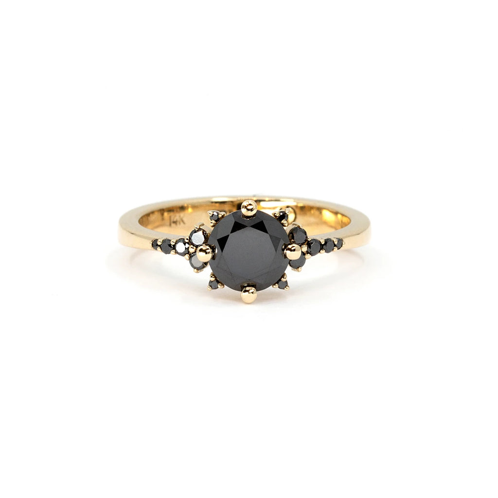 The Éclipse ring, a striking black diamond creation in 14k yellow gold. Featuring a bold round-cut black diamond at its center, surrounded by a delicate constellation of smaller black diamonds and golden bead accents. Available at Ruby Mardi, an independent jewelry boutique in Montreal. Custom jewelry services also offered.