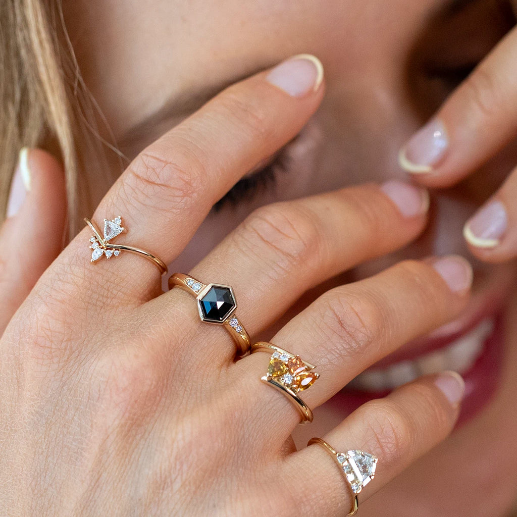 Close-up of a hand wearing multiple gold designer rings, including a black hexagonal diamond engagement ring by Yuliya Chorna, available at Ruby Mardi fine jewelry boutique in Montreal.