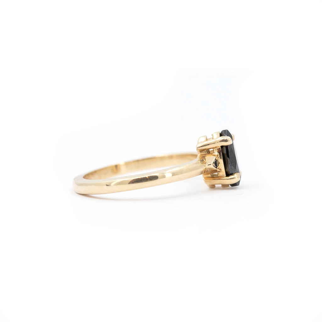 Side view of a yellow gold ring featuring a marquise black gemstone set in hand-carved prongs by Canadian jeweller Liane Vaz.