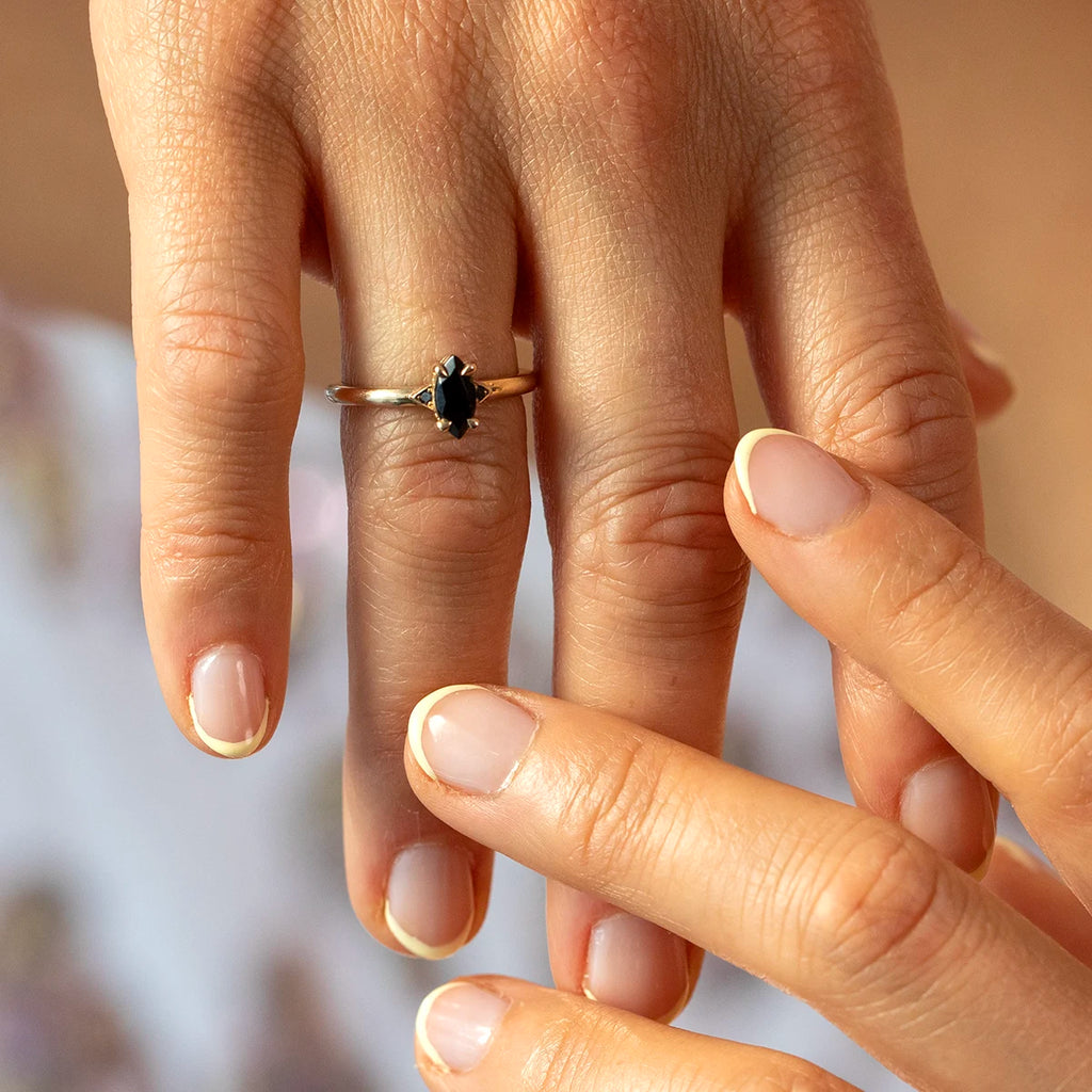 Hand wearing a yellow gold ring with a marquise black gemstone designed by Canadian jeweller Liane Vaz, photographed in natural light.