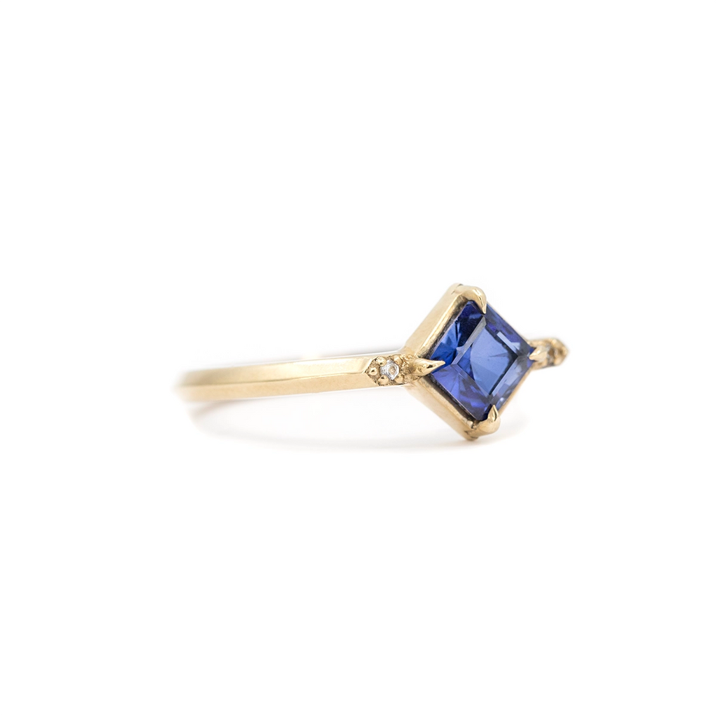 Side view of square blue sapphire ring in yellow gold with small diamond accents, minimalist engagement ring by Liane Vaz for Ruby Mardi.