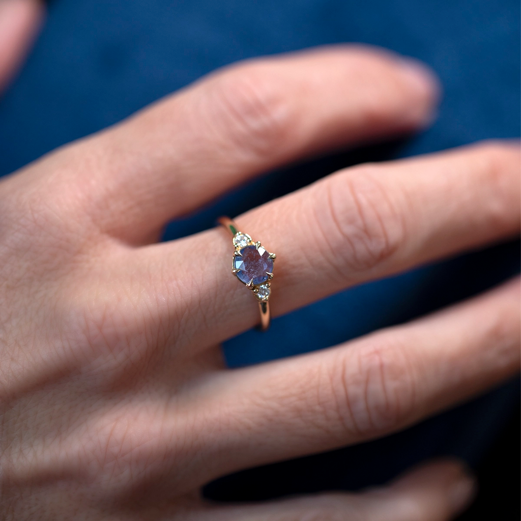 Hand wearing a Rose-Cut Blue Sapphire engagement ring from Ruby Mardi, crafted in Montreal, Canada. Solid 14k yellow gold band with a round blue sapphire and two Canadian diamonds. Shows the low-profile three-stone design and soft natural light on the gemstone.