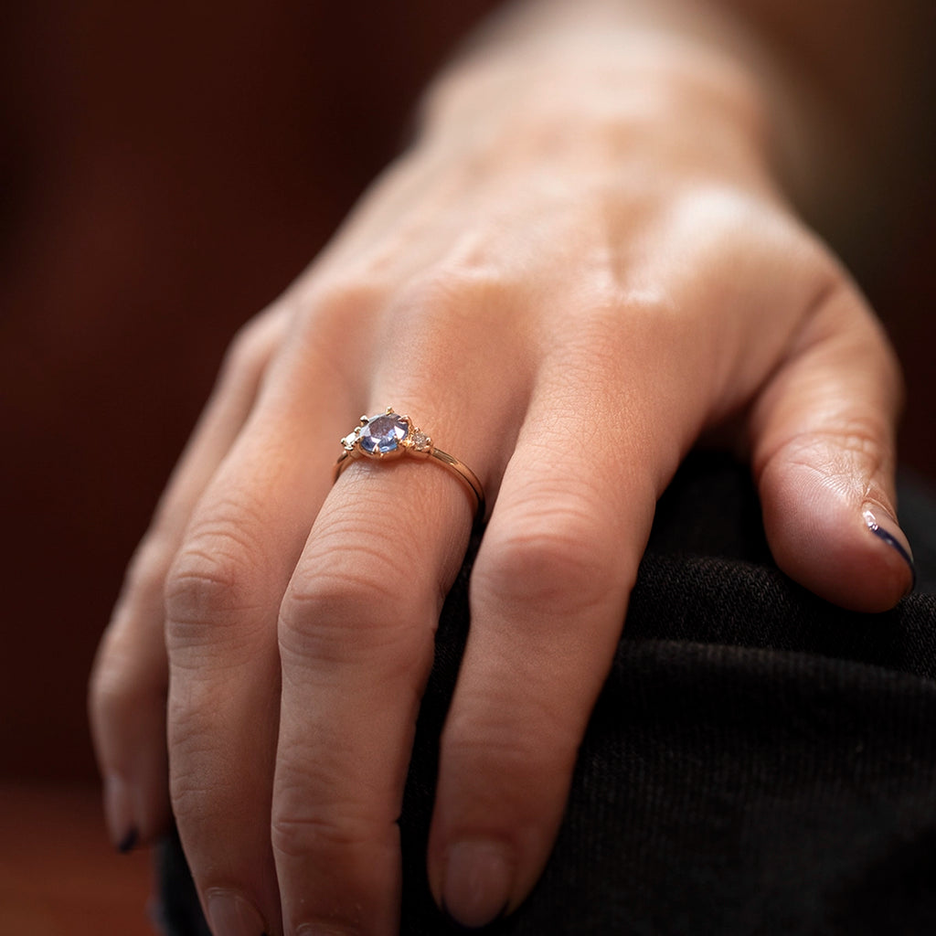 Lifestyle photo of a natural rose-cut blue sapphire engagement ring by Yuliya Chorna, available at Ruby Mardi in Montreal, Canada. Solid 14k yellow gold with Canadian diamonds on each side of the centre stone. Worn on a hand resting on a knee, highlighting the elegant silhouette and handcrafted details.