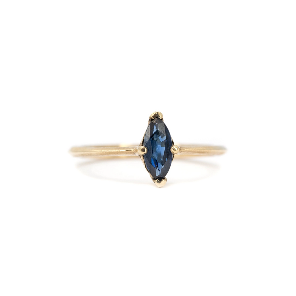 Marquise blue sapphire solitaire ring in yellow gold with minimalist band, fine jewelry by Liane Vaz for Ruby Mardi, photographed on white background