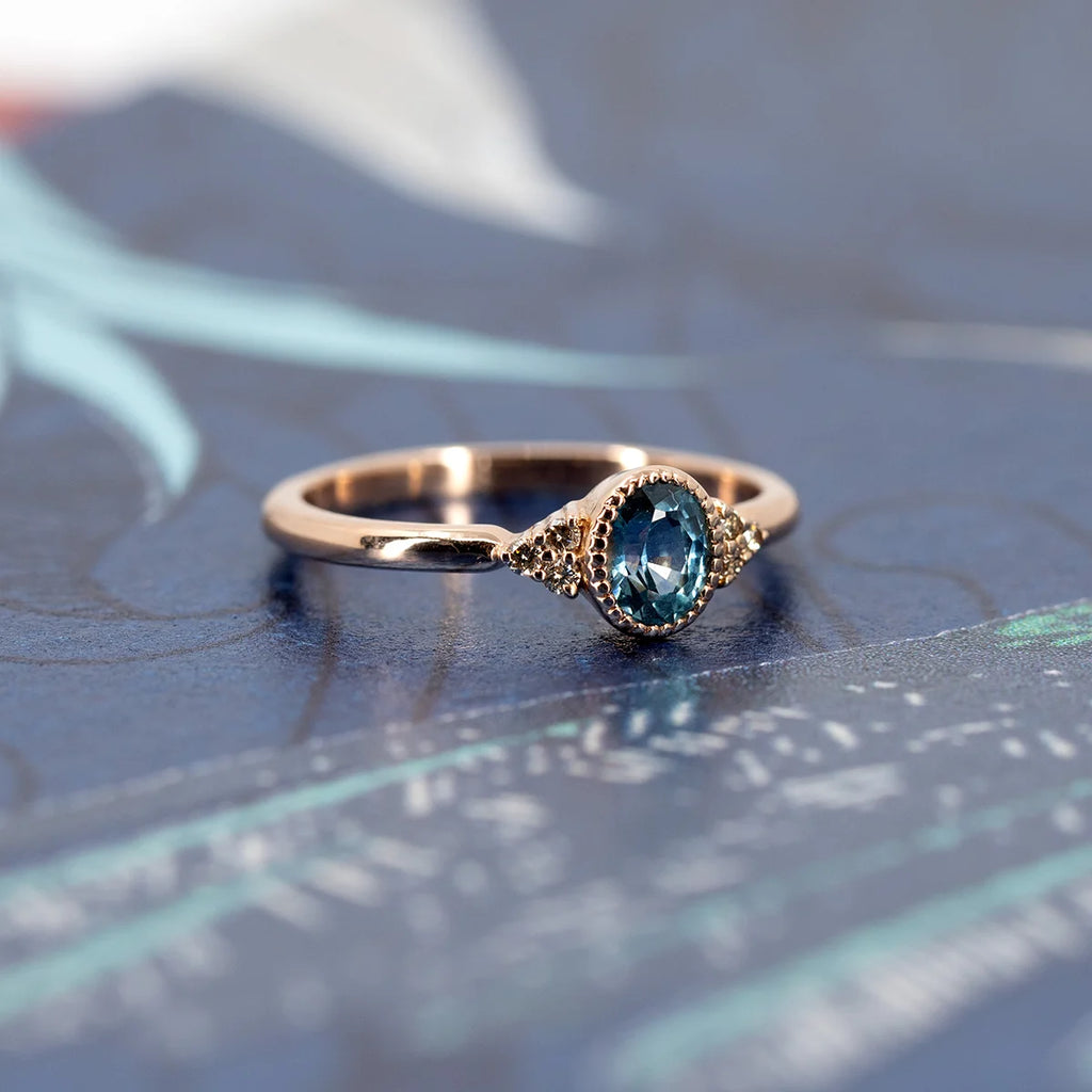 Rose gold engagement ring with an oval blue sapphire and delicate milgrain details, handcrafted by Emige in Montreal, available at Ruby Mardi Jewelry.