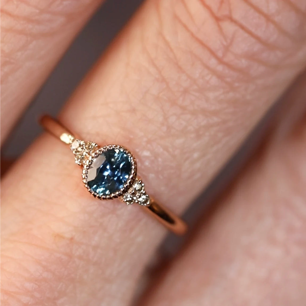 Close-up of a delicate 18k rose gold ring by Atelier Émigé, set with a blue sapphire and Canadian diamonds, available at Ruby Mardi in Montreal.