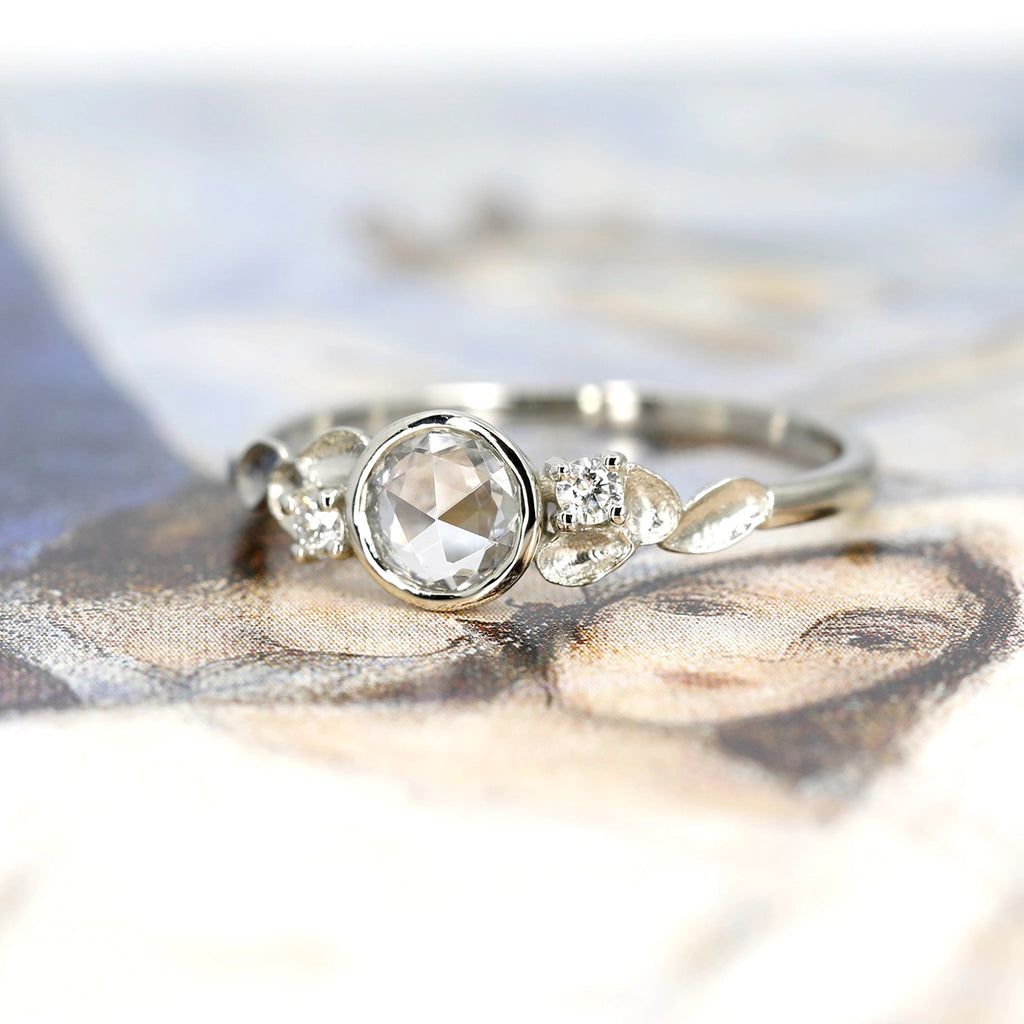 This stunning engagement ring is made with a rose cut white sapphire with small diamonds and a delicate flower motif on the white gold band. Ruby Mardi jewelry specializes in bridal jewelry and wedding rings made by Canadian and independent jewelry artisans.