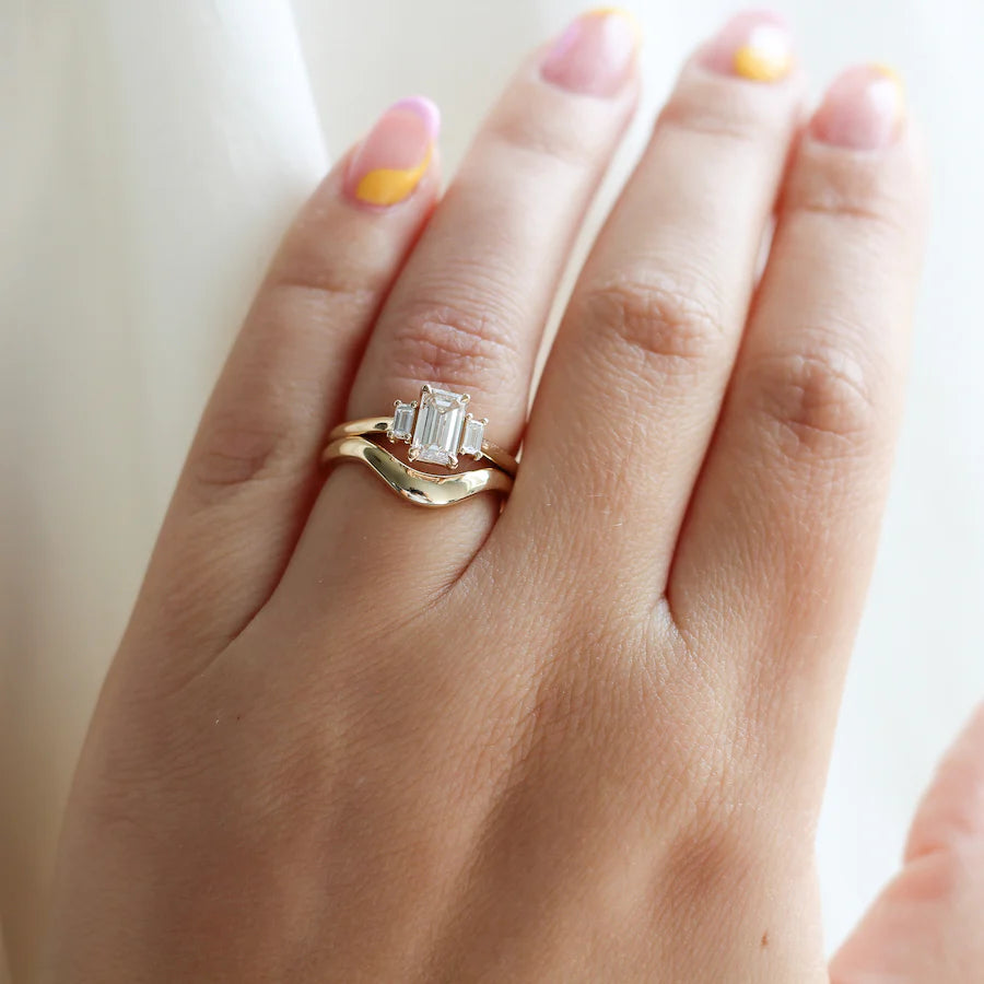 Gold wave wedding band stacked with an emerald-cut diamond engagement ring, designed by Canadian jeweller Yuliya Chorna. Available at Ruby Mardi in Montreal.