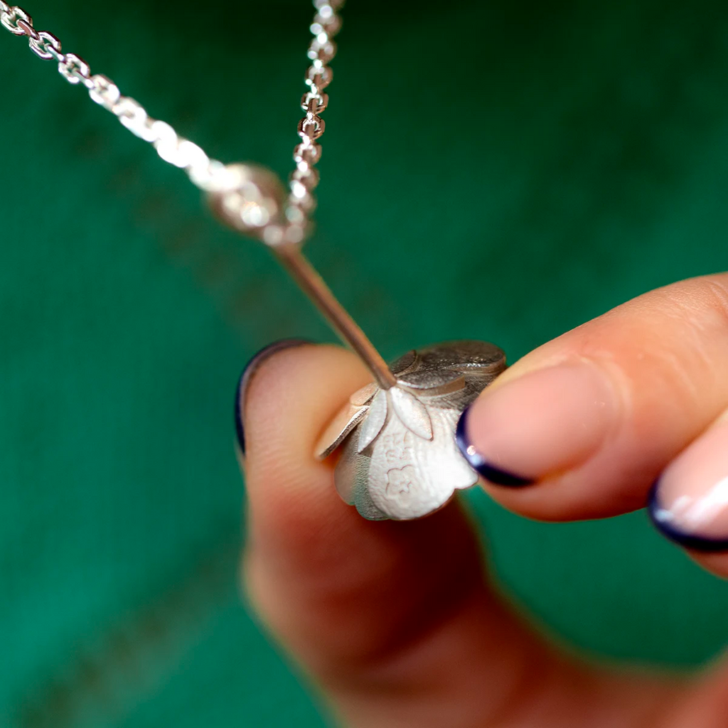 Close up of a white gold buttercup pendant by Fleurs Sauvages Qc, showing the textured petals and stem detail. Nature inspired designer jewelry available at Ruby Mardi in Montreal.