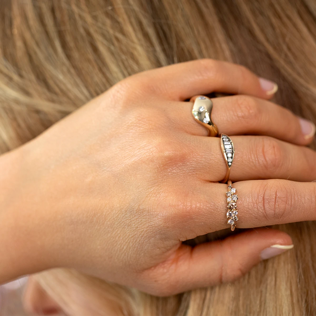 Close-up of a hand wearing three gold designer rings, including a champagne diamond cluster ring, available at Ruby Mardi, a fine jewelry boutique in Montreal.