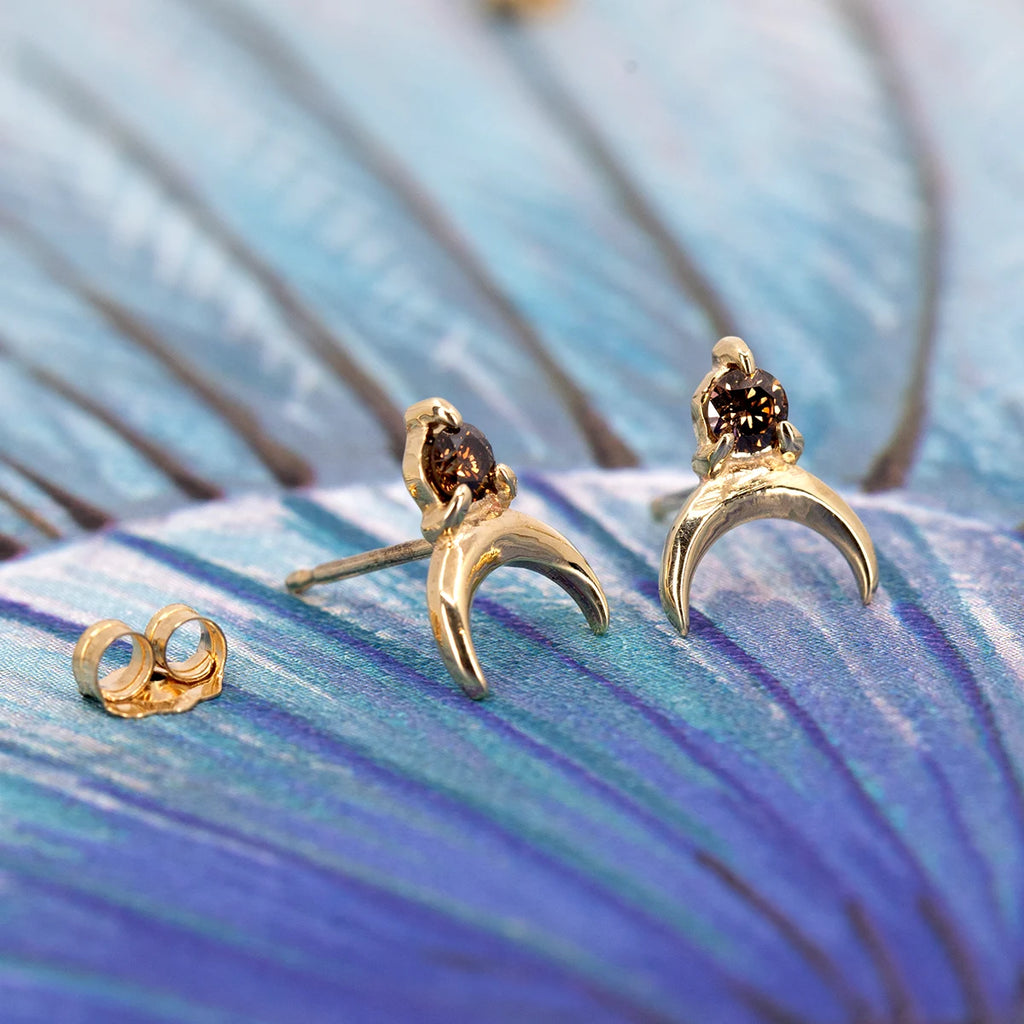 Close-up of chocolate diamond crescent studs in 10k gold, shown on a decorative blue surface, handcrafted by Nadia Werchola.
