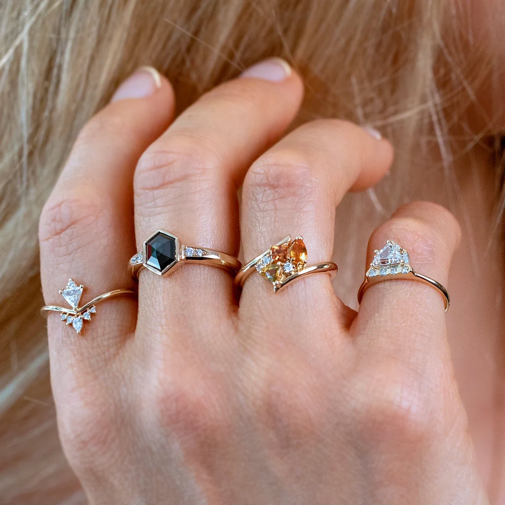 Close-up of a hand wearing four gold designer rings with unique gemstones, including orange, black, and white diamonds, handcrafted by Canadian jewelers and available at Ruby Mardi in Montreal.